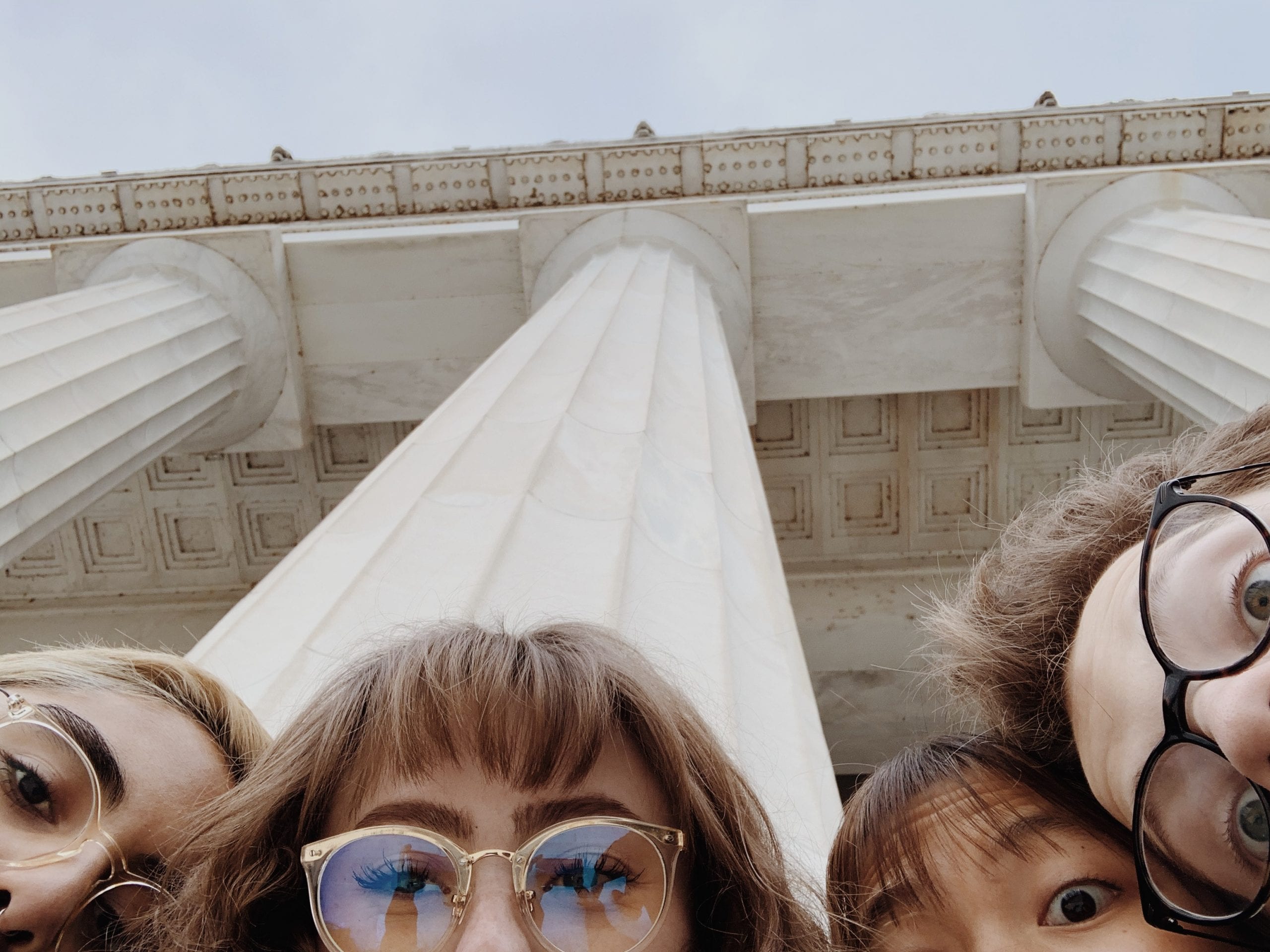 Four students' heads in front of large, white pillars. 