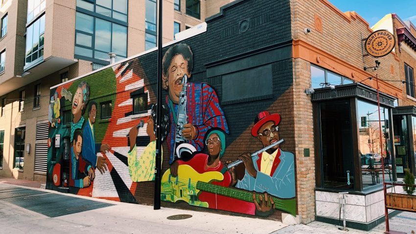 A colorful mural at the side of a building with several musicians playing the saxophone, piano, flute, and guitar