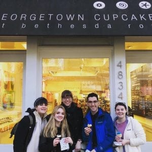A group holds cupcakes in front of the Georgetown Cupcake building.