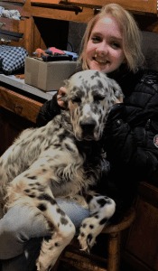 An individual hugs a black and white speckled dog on her lap.