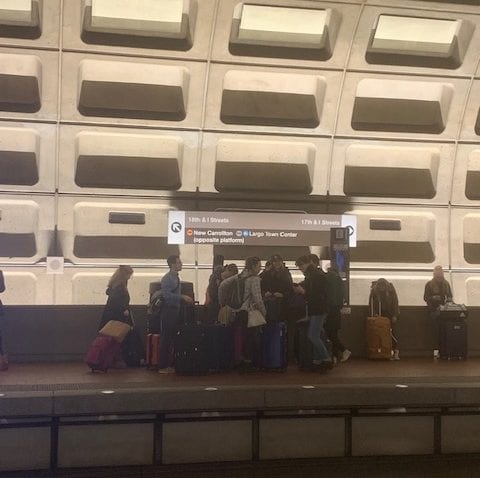 A group stands with suitcases on a metro platform