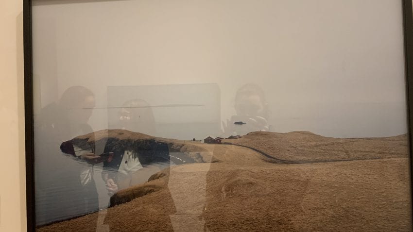 The reflections of two individuals in the glass cover of an art exhibit. 