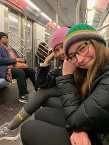 Two girls in colorful hats sit on a subway. 