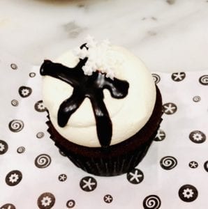 A chocolate cupcake with vanilla frosting and a black chocolate bowtie. 