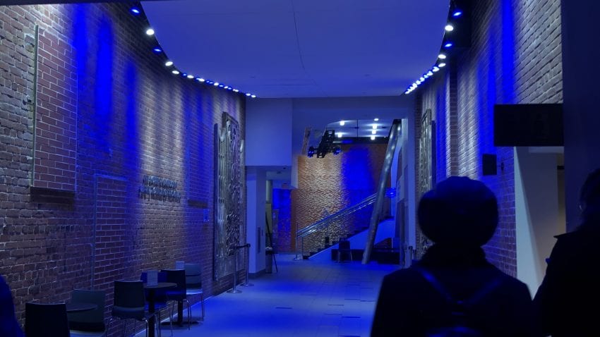 A brick hallway with blue lighting leads to a stairway 