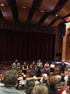 Composers stand at the front of a theater for a talkback. The seats are filled with audience members.