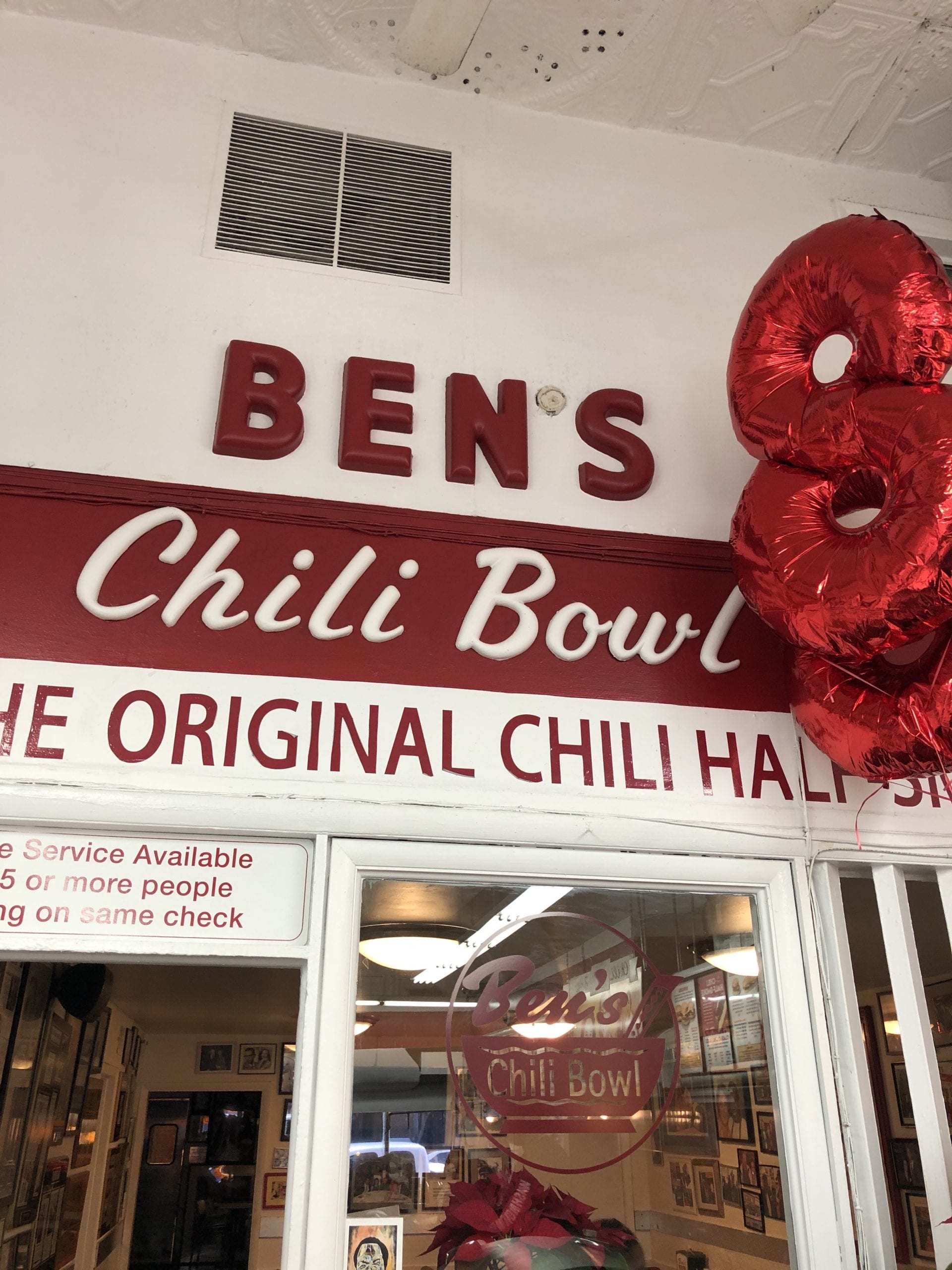 The front of a white building reading "Ben's Chili Bowl" in red on top of a glass window and door