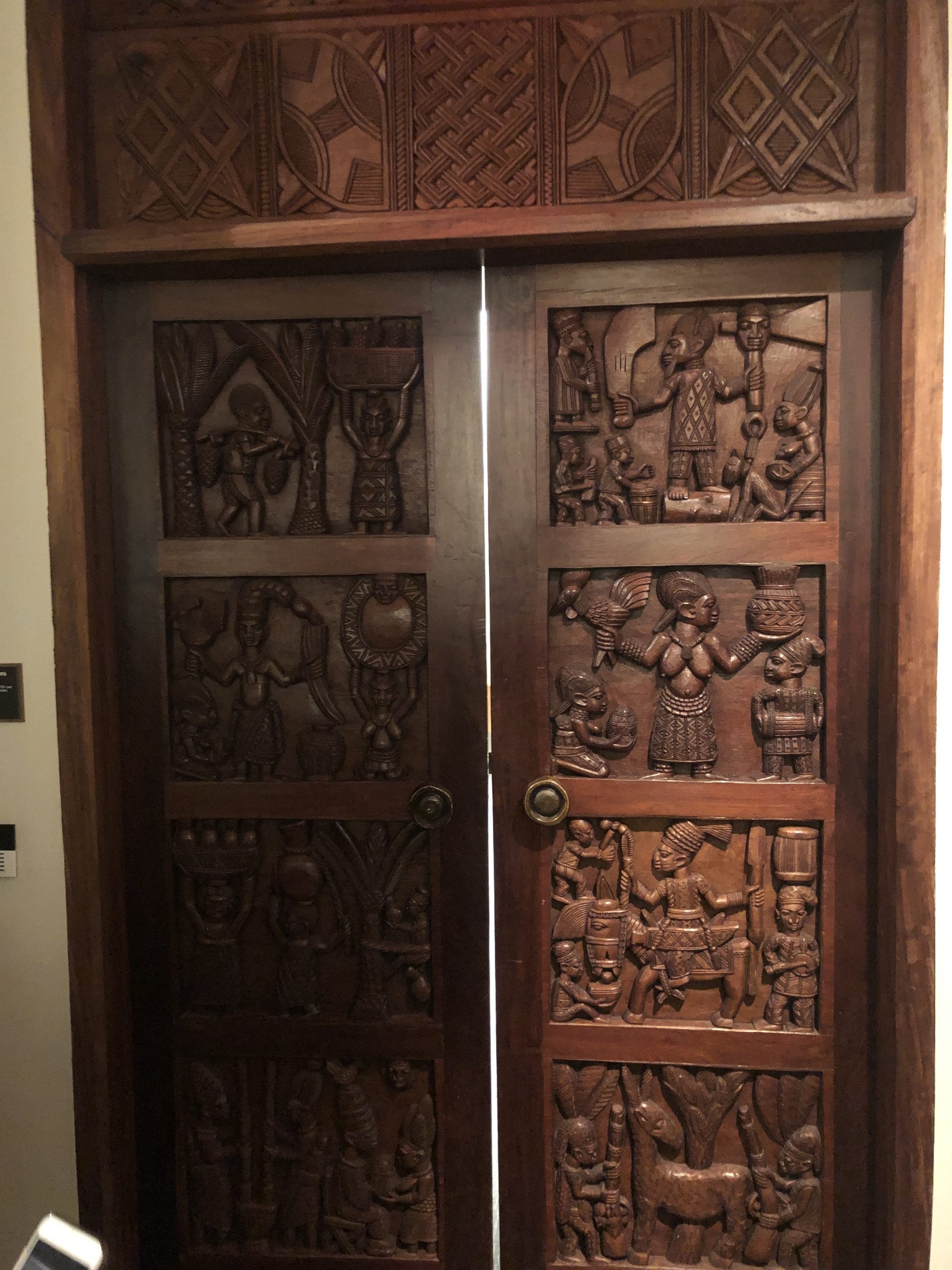 A wooden door with carved images of people working and playing instruments