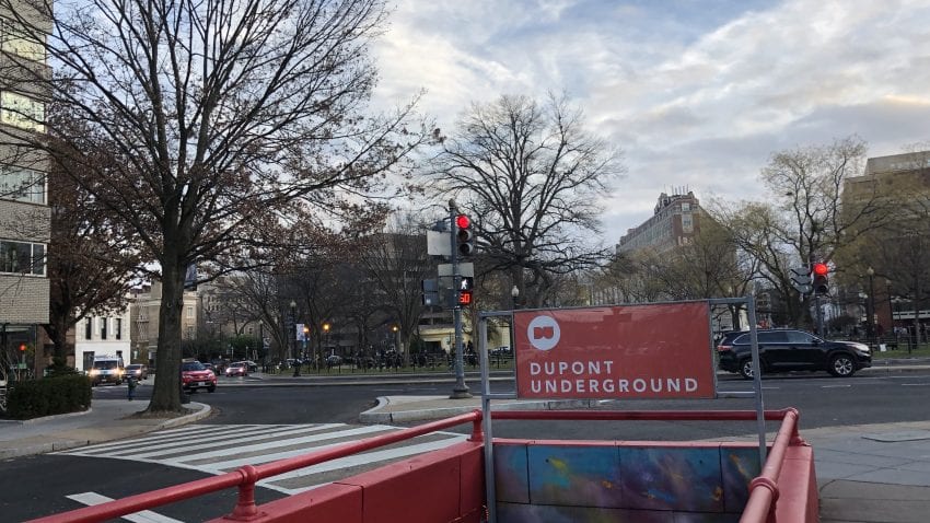 The entrance to Dupont Underground - a red poster with the title and stairs leading down to the organization. It is surrounded by a busy street circle.