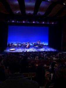 An image of a stage with a small orchestra and space in front of the instrumentalists for performers. The stage features a blue background.
