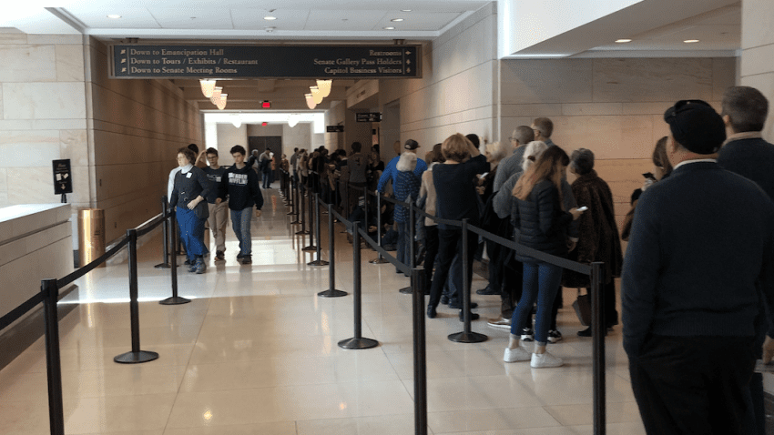 A line of people on the right side of a hallway with black ropes separating the line 