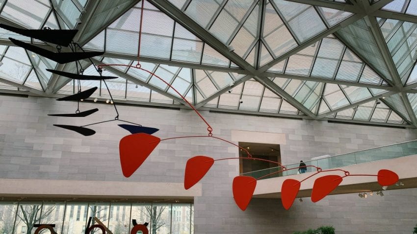 Red and black triangles hang from a ceiling. Square pieces of glass make up the ceiling.