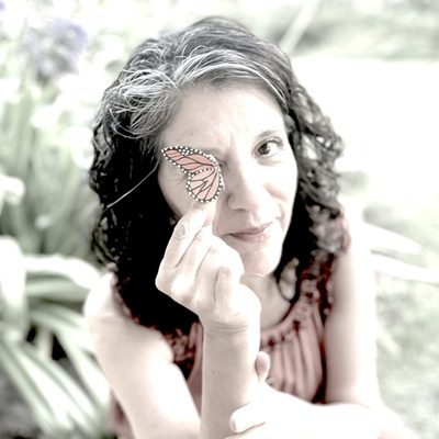 Latina woman holding a mariposa in front of her face.