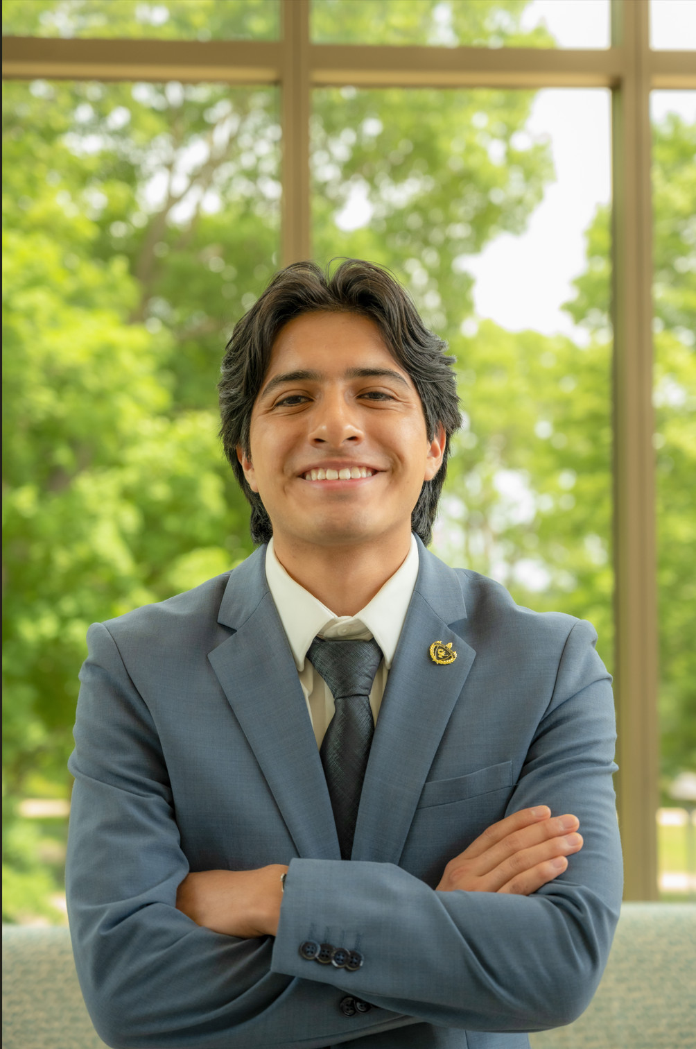 Young Latino guy with a suit smiling to the camera.
