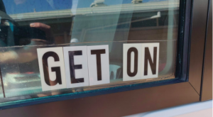 A photo of our bus driver's window saying "GET ON"